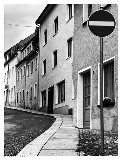 Aufnahme in schwarzweiß, eine schmale Gasse in Wolkenstein/Erzgebirge, rechts mehrere aneinander gebaute kleine Häuser und ein rundes Verkehrszeichen (Durchfahrt verboten)