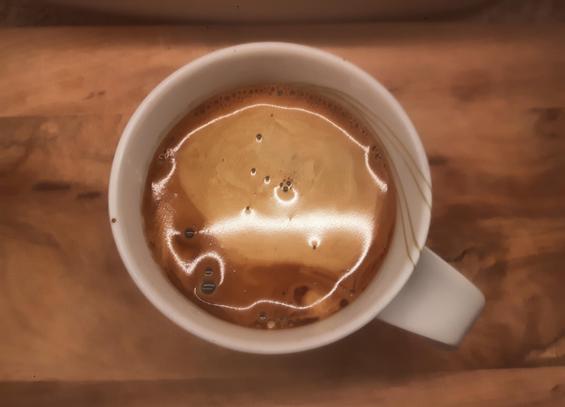 Eine Tasse Americano, von oben fotografiert, auf einem Holzbrett.