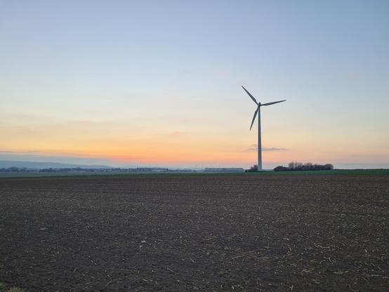 Sonnenuntergang, davor ein Windkrad und ein kahles Feld