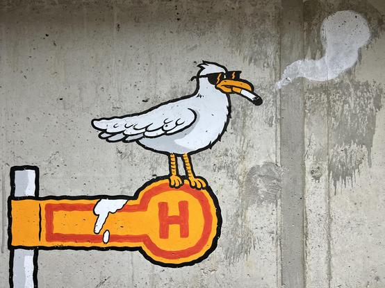 Graffiti an einer Betonwand: Möwe mit Sonnenbrille und Zigarette steht auf Haltestelle-Schild