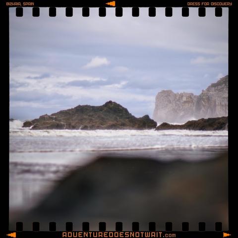 A dramatic coastline in Bizkaia, Spain, where crashing waves meet rugged cliffs under a moody sky, inspiring organic adventure apparel and sustainable outdoor clothing. The raw power of the Basque Coast captured in nature-themed designs.