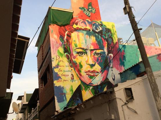 Ein lebendiges Wandbild mit einem farbenfrohen Porträt einer Frau mit unverwechselbaren Haaren und Accessoires. Das Kunstwerk enthält Text auf Spanisch, und die umliegenden Gebäude sind teilweise sichtbar. Die Szene fängt die Essenz der Straßenkunst in einer städtischen Umgebung ein.

A vibrant mural featuring a colorful portrait of a woman with distinctive hair and accessories. The artwork includes text in Spanish, and surrounding buildings are partially visible. The scene captures the essence of street art in an urban setting.