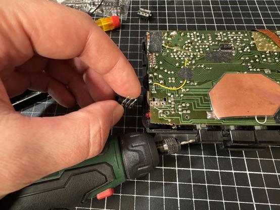 Internal view of an old walkman. Larger holes have just been drilled on the PCB. A hand is holding a new jack connector.