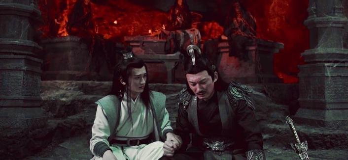 Nie Huaisang sits beside Nie Mingjue in an ominously red lit cavern, tightly holding Mingjue's right hand in his own left hand and looking at the his older brother with concern while Mingjue appears to be struggling under an emotional burden.
