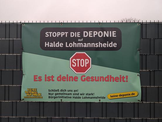 Plakat an einem Zaun: "Stoppt die Deponie auf Halde Lohmannsheide. Es ist deine Gesundheit! Schließ dich uns an! Nur gemeinsam sind wir stark! Bürgerinitiative Halde Lohmannsheide. www.keine-deponie.de