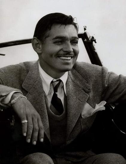 A black and white portrait photograph depicts a person in formal attire, likely taken mid-20th century. The individual is seated and looking slightly off to the side with a warm smile. They are wearing a patterned suit jacket, a vest, a collared shirt, and a dark tie, with a pocket square visible in the jacket's breast pocket. The person’s left hand is resting on their leg, featuring a ring on their finger. A portion of what appears to be a vehicle's interior, including a dark metal rod, is visible in the upper right corner of the frame.
Provided by @altbot, generated privately and locally using Gemma3:27b
