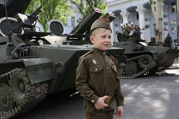 A boy wearing a Soviet-era uniform standing in front of an APC during rehearsal of Victory Day parade in Russian occupied Donetsk.