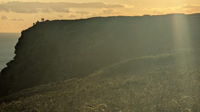 An image of distant walkers silhouetted on a cliff top, with the sun setting behind them.