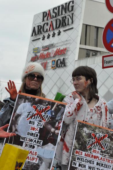 Aktivisti mit Plakaten: Fast Fashion durchgestrichen, darunter harte Fakten:

- Bis zu 30% Ihrer Neuware wird niemals verkauft
- 35% des Mikroplastiks welches derzeit in den Weltmeeren schwimmt stammt aus Kleidung