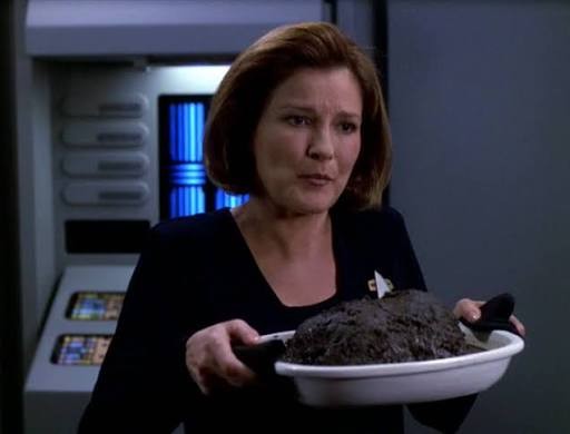 Janeway holding up a burnt roast that looks like a giant lump of charcoal