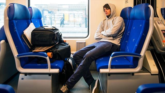 Ein junger Mann sitzt schlafend in einem Zugabteil, während sein Gepäck auf den Sitzen ihm gegenüber liegt. Sind Sitzplatzreservierungen für Taschen und Rucksäcke erlaubt? (Foto: IMAGO, IMAGO / Dreamstime)