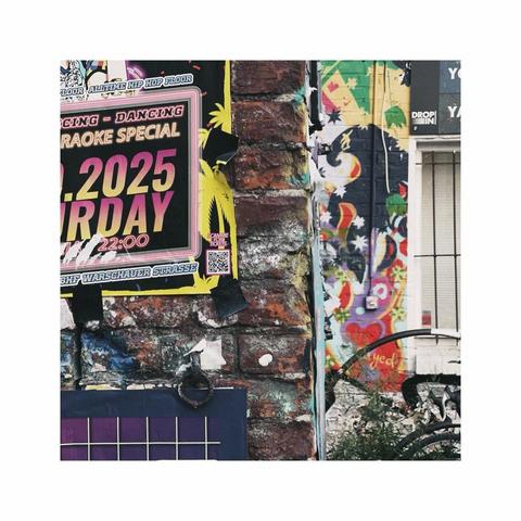 a square image presenting a smal detail of the corner of a brick wall. there are graffitis, murals, posters and stickers all over the place