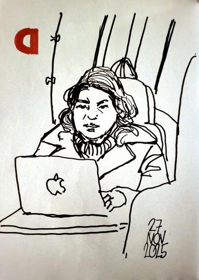 Kvinna i kappa på tåget. Sitter vid ett bord och skriver på sin laptop.