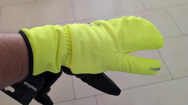 Photo of my left hand in a yellow left glove that looks weird because only thumb and index finder have a solo place, the other three fingers are together, for more warmth. The gloves are neon yellow.