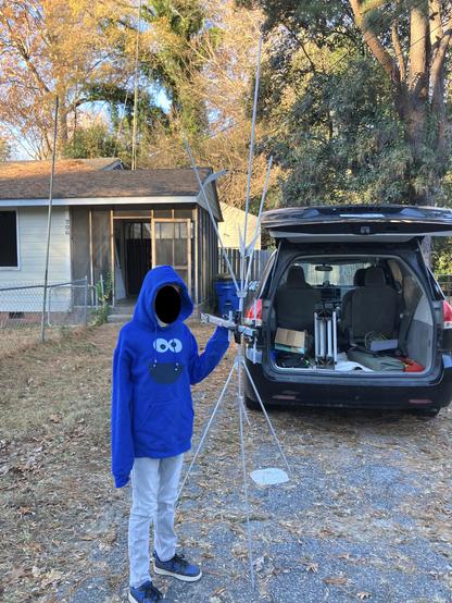 a boy in a Cookie Monster shirt holding an antenna in front of a dilapidated house