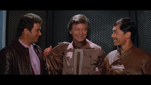 A shot from Star Trek III: The Search for Spock showing Kirk, McCoy and Sulu in a turbolift.  Kirk is grinning and McCoy and Sulu are smiling.