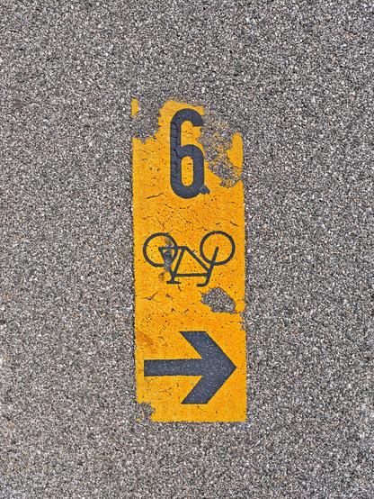 Gelb auf den Asphalt gedruckt ein Hinweis: 9, Fahrrad, Pfeil nach links. Das Photo steht auf dem Kopf.