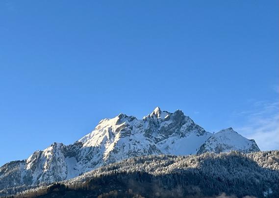 Pilatusberg, verschneit, vor praktisch wolkenlosem blauen Himmel. Die Sonne bescheint den Berg von links. Die bewaldeten Hügel vor dem Berg sind ganz oben leicht mit Schnee