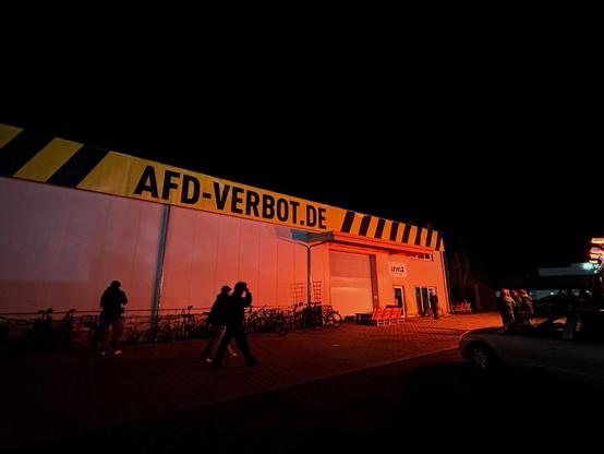 Gewerbehalle mit riesiger Dekoration im Stil eines Absperrbandes in Schwarz und Gelb zeigt den Schriftzug AFD-VERBOT.DE bei Nacht