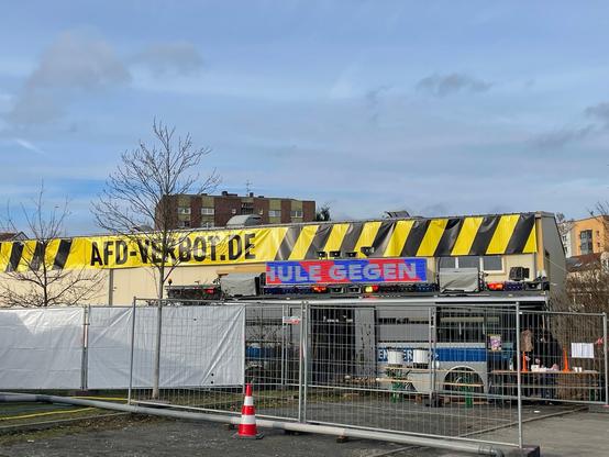 Gewerbehalle mit riesiger Dekoration im Stil eines Absperrbandes in Schwarz und Gelb zeigt den Schriftzug AFD-VERBOT.DE bei Tageslicht