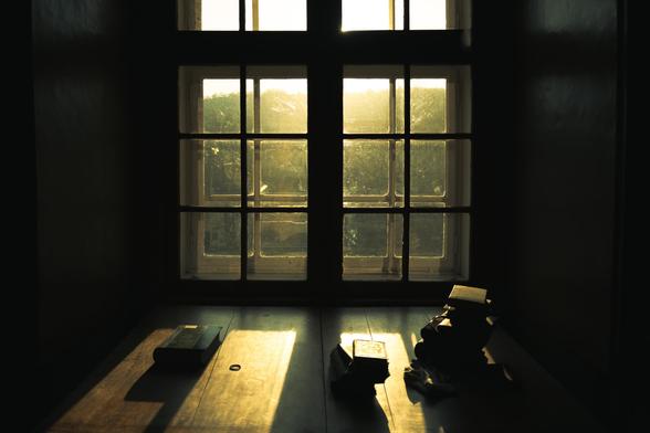 Photo of a window taken at Stift Klosterneuburg. The window was inside the library section. The photo has a stark contrast of golden light coming in, shining onto an old table with a few books on it