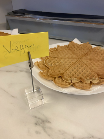 Two Norwegian-style waffles on a plate and a sign in front that says “Vegan”.