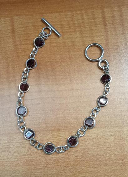 A bracelet made of argentium silver and garnets. The square silver wire is wrapped around each flat garnet bead and the joined via welded jump rings. The clasp is a simple toggle.
