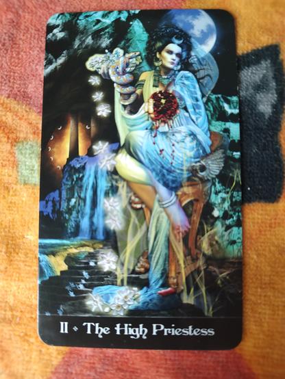 Card from the Tarot Apokalypsis deck. 
The High Priestess-II.
A woman seated on a stool, wearing white robes, seated in a cave entrance, a full moon in the sky above.