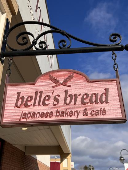 Photo of a hanging wood sign. It is pink and reads “Belle’s Bread, Japanese bakery and cafe.”