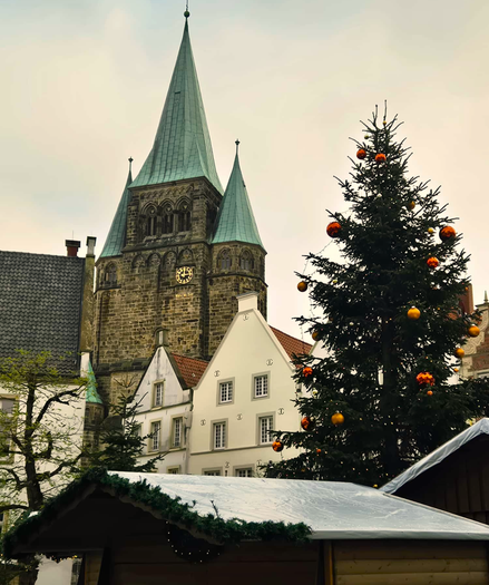 Blick über Dächer eines Weihnachtsmarktes zu Hausgiebeln und den Türmen einer Kirche