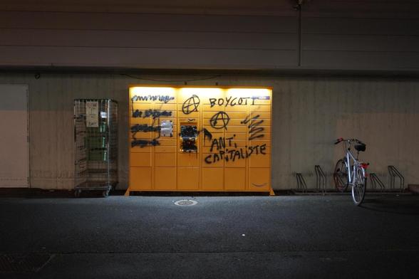 Photo d'un locker Amazon la nuit. Il est tagué avec de la peinture noir, et l'écran est recouvert de peinture noir.