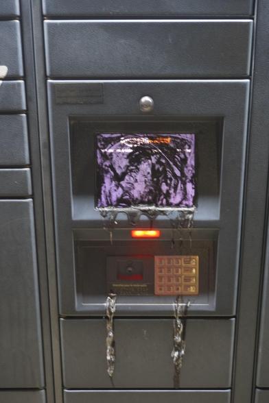 Photo en gros plan de l'écran d'un locker amazon recouvert de peinture noir dégoulinante.