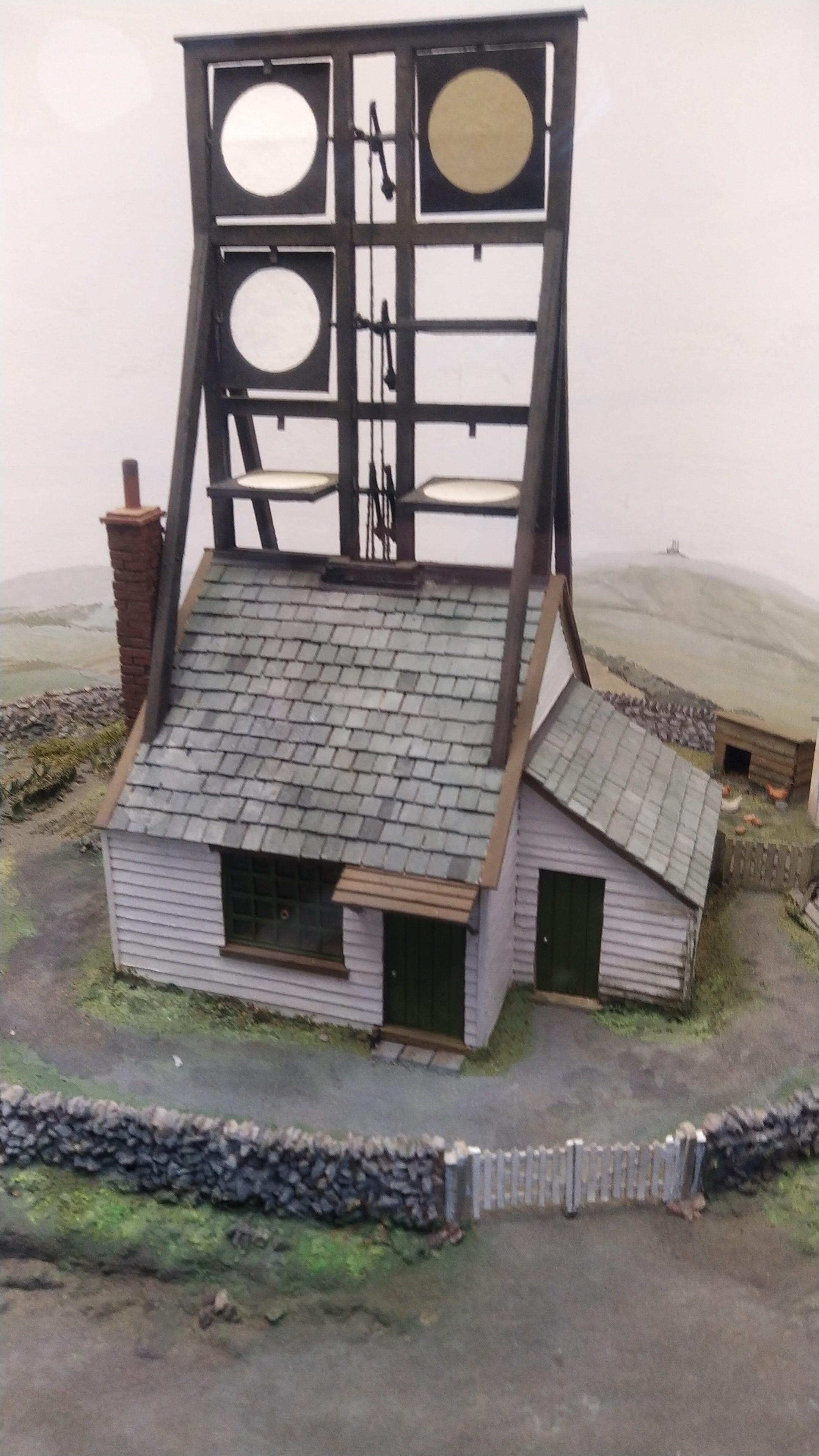 A model.of a shutter tower..It comprises a single storey building topped by a rectangular wooden frame about 1.5x as high as the building. The frame is divided into a 3 high x 2 wide grid by slats, and each place in the grid has a shutter than rotates around its central horizontal axis to open and close.