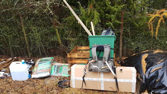 An einem rucksackartigen Metallgestell befestigt ein großer Karton, ein großer Plastikbehälter mit Geräten und Baumbusstäben darin. Daneben Säcke mit Gartenkompost und ein nicht voller 20-l-Wasserkanister. Außerdem Kompost, Schwarze-Plastikplanen-Lager, hintendran ein Metalldrahtzaun.