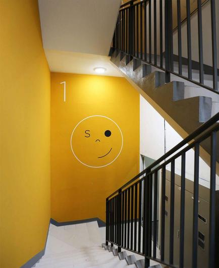 A brightly painted yellow stairwell features a playful smiley face and the number "1" on the wall, with a metal railing and steps visible.