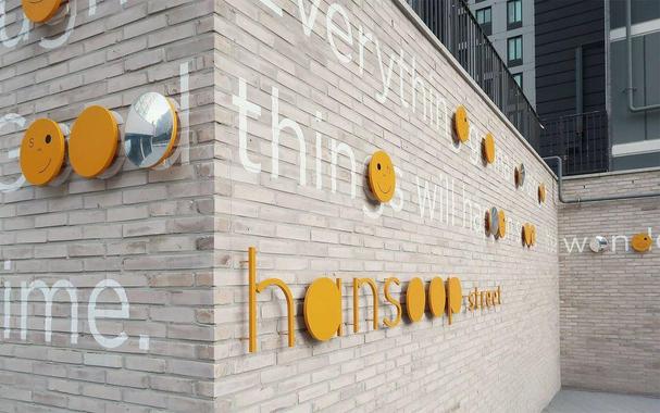 A brick wall displays cheerful yellow smiley faces and orange text spelling "hansoop street" alongside white inspirational phrases.