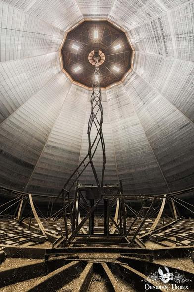 inside a huge cylinder, light coming in top. a long zig zag ladder reaches up