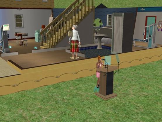A virtual scene showing two characters in a house setting. One character is standing at a podium, speaking, while another character in a plaid skirt stands nearby. The background features stairs and various household items.