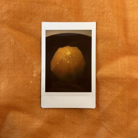 Instant photo of a pealed orange ball in a black bowl on a orange texture background.