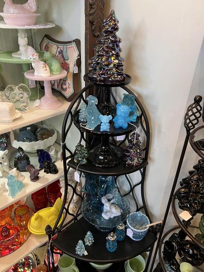 Photo of a multiple layers shelf with various carnival glass pieces on it, several of which are Christmas trees. In the background more glass can be seen on shelves.