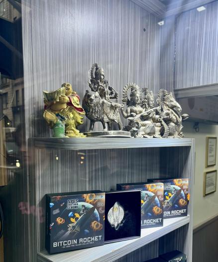Top shelf, different Hindu gods, in silver I assume. Second shelf, color boxes holding silver shaped space craft, named the Bitcoin Rocket.