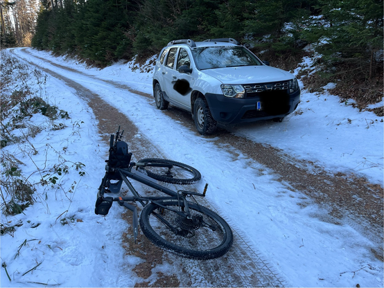 SUV im Wald. Vorne ein Fahrrad. Gut gepflegte breite Forststrasse