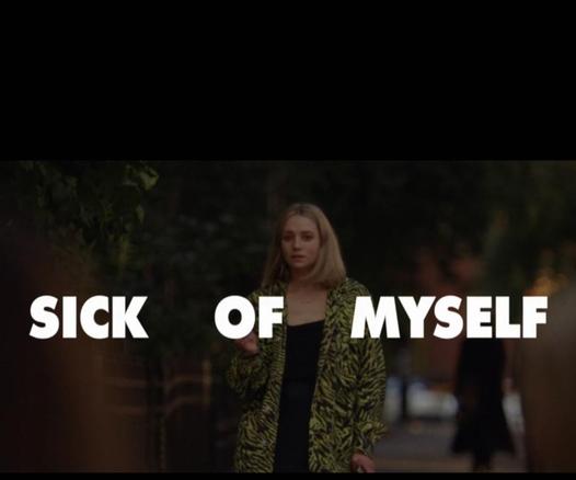 Image is photo still from the film "Sick of Myself". Pictured is a Norwegian woman standing on the sidewalk with large, white text across the image. Text reads: SICK OF MYSELF.