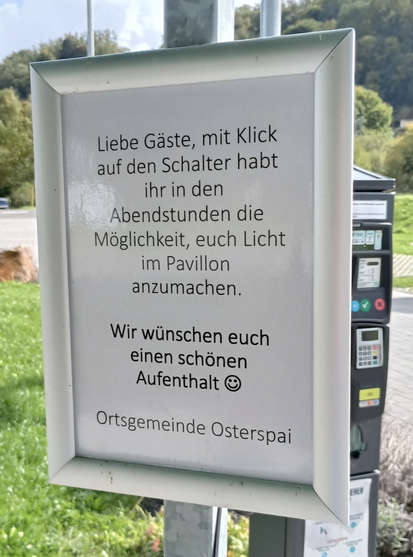 Sign that says (in German) "Dear guests, with a click of the button you have the ability to turn the pavilion lights on during the evening hours. We wish you a pleasant stay, Ortsgemeinde Osterspai".