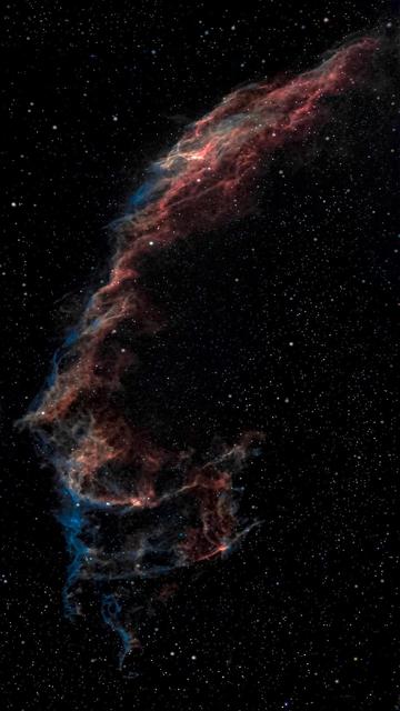 Żywa kosmiczna scena z kolorową mgławicą otoczoną niezliczonymi gwiazdami. Mgławica wyświetla odcienie czerwieni, błękitu i pomarańczy, na ciemnym tle przestrzeni.