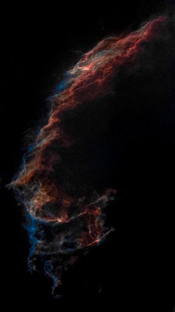 Eteryczna mgławica z wirującymi chmurami w odcieniach czerwieni i błękitu, na czarnym tle, przypominająca kosmiczny pióropusz.
