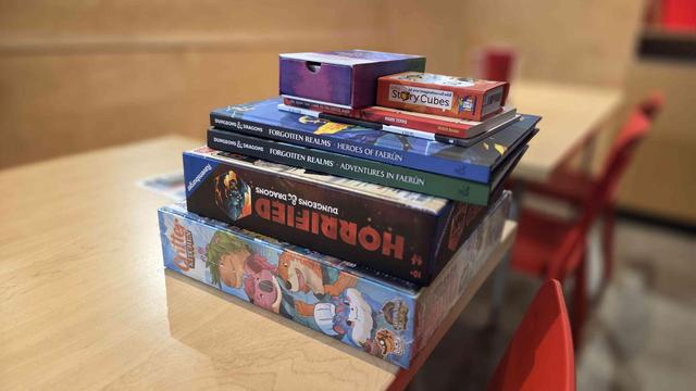 A photo of a pile of games and books on a wood table, awaiting purchase.