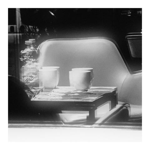 Doppelte Spiegelung eines Tisches mit Tassen und Flasche und mit einem Sessel