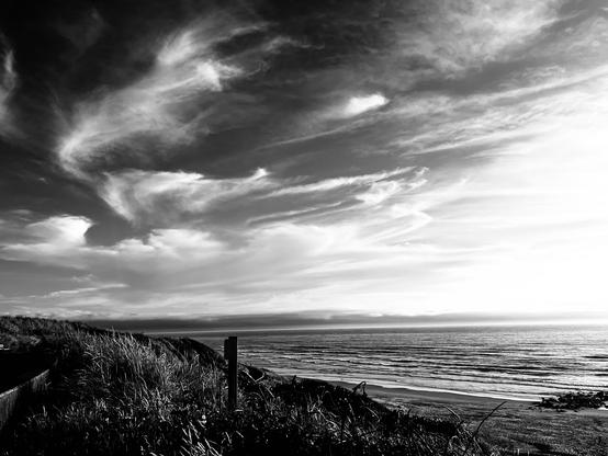 A striking black and white photo of wispy clouds over a calm sea. Photo by Robert Emond.