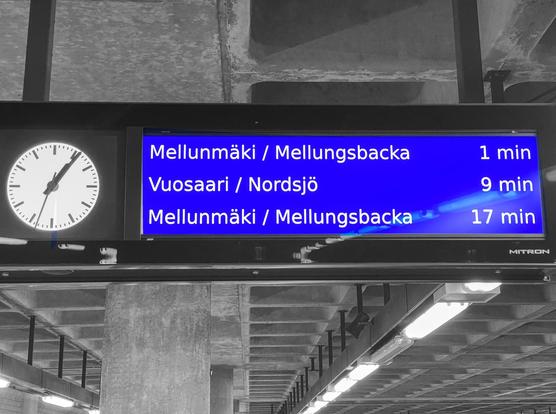 Metroaseman aikataulunäyttö. Kello on 1.06. Mellunmäki / Mellungsbacka 1 min, Vuosaari /Nordsjö 9 min, Mellunmäki / Mellungsbacka 17 min. Taustalla aseman katon betonirakenteita.